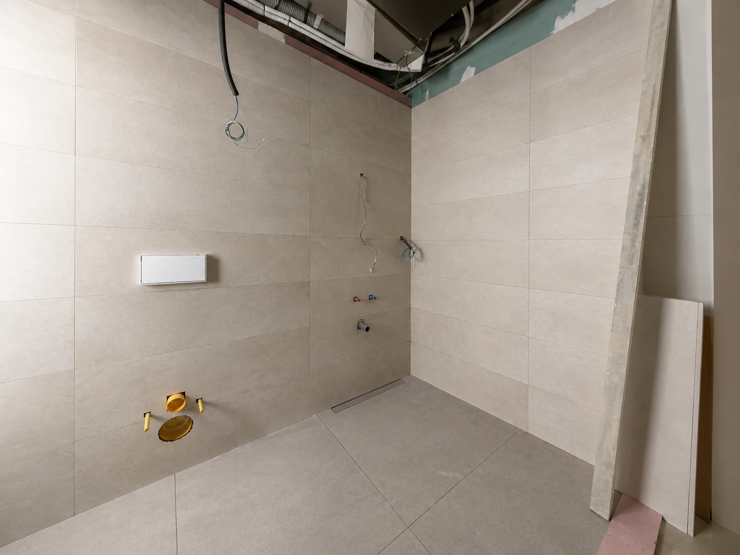 Baño en fase de obra con alicatado parcial, canaleta de desagüe y materiales de construcción en el suelo.